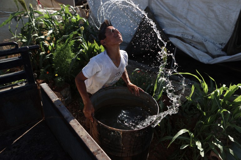 A Syrian youth cools off as he dips his head in a water barrel at a camp for internally displaced people (IDP) near Sarmada, in the northern Syrian province Idlib on June 28, 2024. - After 13 years of civil conflict, lack of international funding has severely undercut the provision of basic services such as water, waste disposal and sanitation in displacement camps in northwest Syria, according to the United Nations. More than five million people, most of them displaced, live in areas outside government control in Syria's north and northwest, according to the UN, many relying on aid to survive. (Photo by AAREF WATAD / AFP)