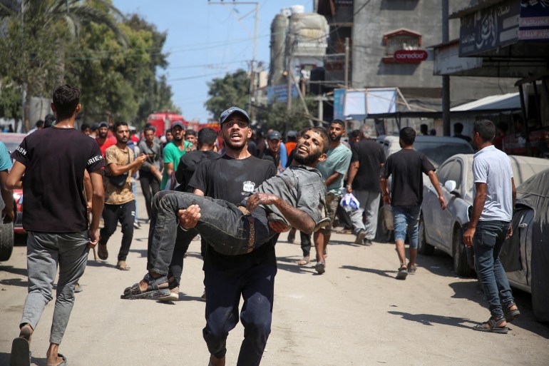 A Palestinian carries an injured man at the site of what Palestinians say was an Israeli strike at a tent camp in Al-Mawasi area, amid Israel-Hamas conflict, in Khan Younis in the southern Gaza Strip July 13, 2024. REUTERS/Hatem Khaled