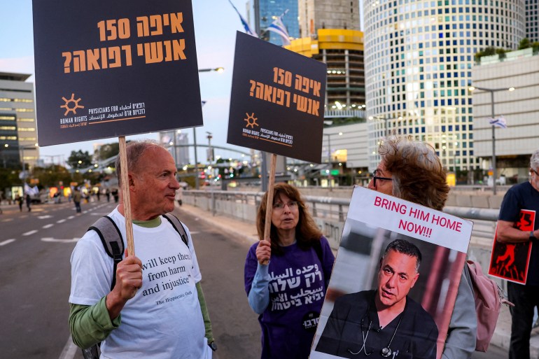 A demonstrator holds a sign depicting Israeli-detained Palestinian paediatrician Hussam Abu Safiya, director of the Kamal Adwan Hospital in northern Gaza's Jabalia, while standing with others gathering during an anti-government protest against the death of Gaza aid workers outside the Israeli Defence Ministry headquarters in central Tel Aviv on April 5, 2025. Israeli forces launched a ground offensive in Gaza City, the military said on April 4, after renewed military operations in March ended a short-lived truce in its war with Hamas. Israel has since expanding its operations pushed to seize territory in the Gaza Strip in what it said was a strategy to force militants to free hostages still in captivity. (Photo by Jack GUEZ / AFP)