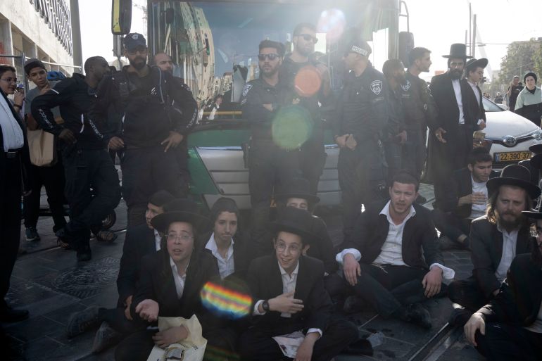 Israeli police stand guard as ultra-Orthodox Jewish men and boys, block a bus from crossing Jaffa Street in central Jerusalem, Thursday, Sept. 29, 2022 to protest attempts to force them to register for Israel's military draft. Military service is mandatory for most Jewish Israeli men, but the ultra-Orthodox often receive exemptions in order to continue their religious studies. (AP Photo/ Maya Alleruzzo)