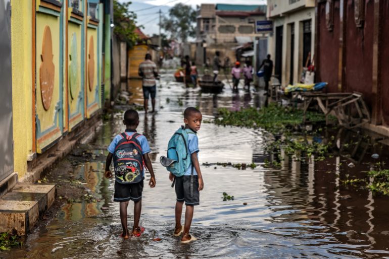 Students carry schoolbags as they walk down a flooded street in Gatumba. [Luis Tato/AFP]