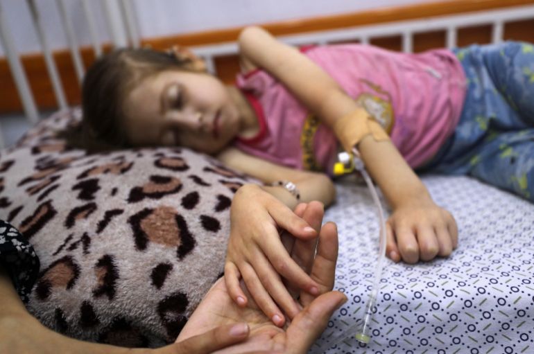 A Palestinian girl Jana Ayad, who is malnourished, according to medics, lies on a bed as her mother, Nasma Ayad, sits beside her, holding her hand, as she receives treatment at a hospital in Gaza City, amid a worsening hunger crisis, July 29, 2025. REUTERS/Mahmoud Issa