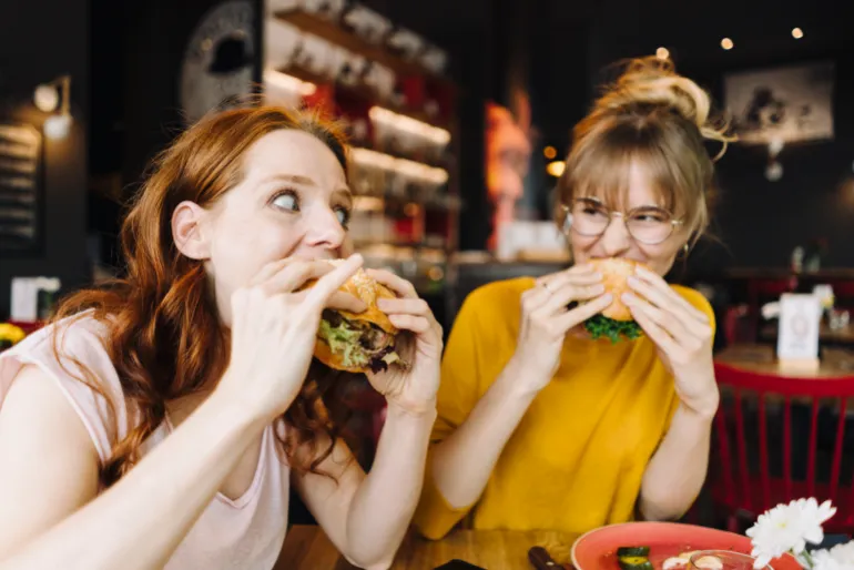 Two female friends eating burger in a restaurant